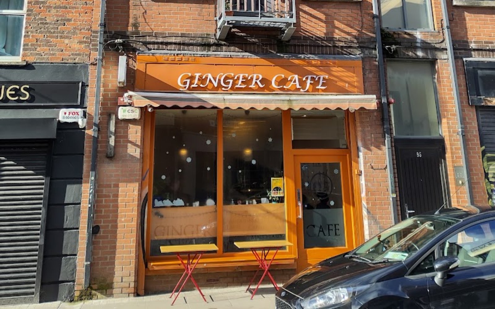 Ginger Cafe's terracotta shopfront on Francis Street, with cream lettering on the fascia, an awning and two small red café tables outside